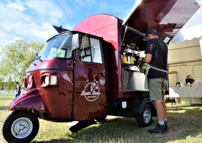 Photo of a coffee shop trailer. A burgundy three wheeled vehicle with the coffee shop built into the back