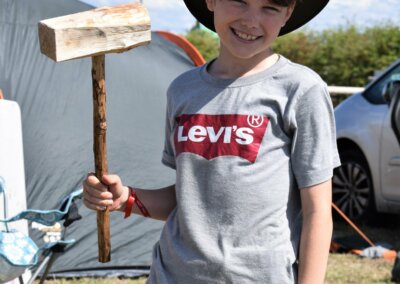 Young boy holding a large wooden mallet while standing next to a tent in a camping field