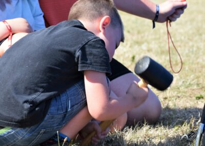 A young child kneeling on the grass and holding a mallet to knock tent pegs in