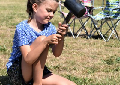 A young child kneeling on the grass and holding a mallet to knock tent pegs in