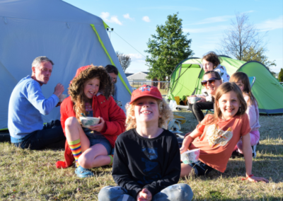 A group of people sat around their tents with three young people at the front smiling for the camera