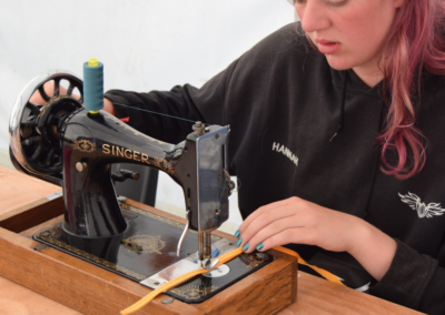 A person sat at a handcrank sewing machine