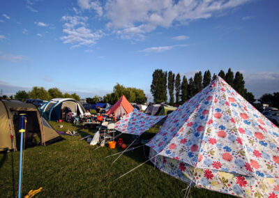 A field of tents with trees in the background and a bright blue sky