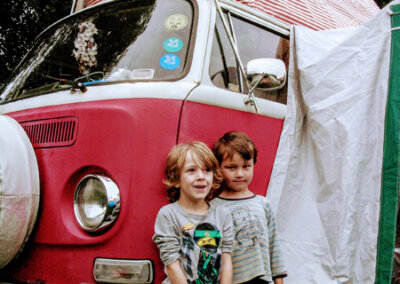 Photo of two young children standing in front of a red VW camper.