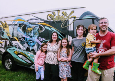Photo of a family stood in front of a painted campervan.