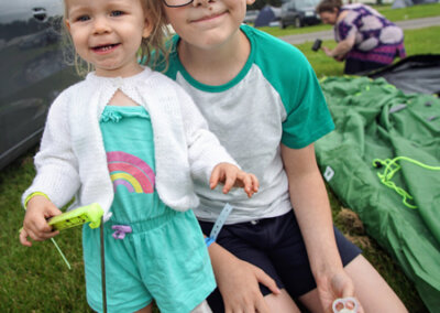 Photo of two children on the grass with a tent being put up behind them