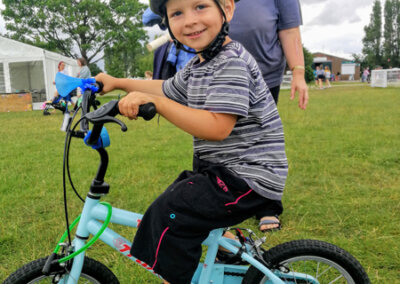 Photo of a young child sat on a blue bike with stabilisers and smiling for the camera
