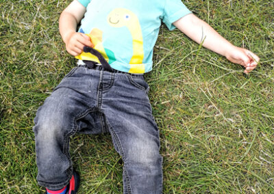 Photo of a young child asleep on the grass with a wide brimmed hat partially covering his face. He looks chilled out and happy