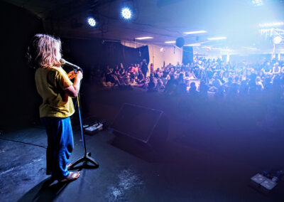 Photo taken from behind of a young person on stage looking out into the audience