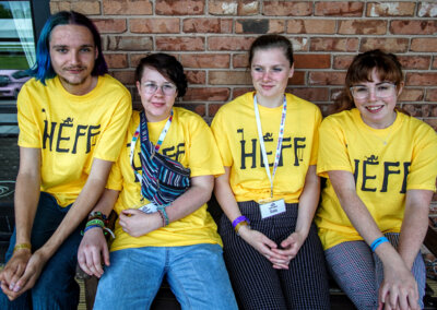 Photo of four young adults sitting on a bench wearing yellow HEFF tshirts