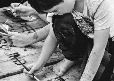 Black and white photo of a young person kneeling down and painting a facemask