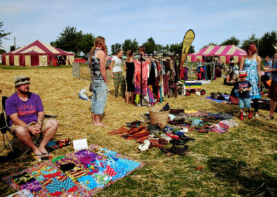Brightly coloured photo of people selling clothing and other items in a field