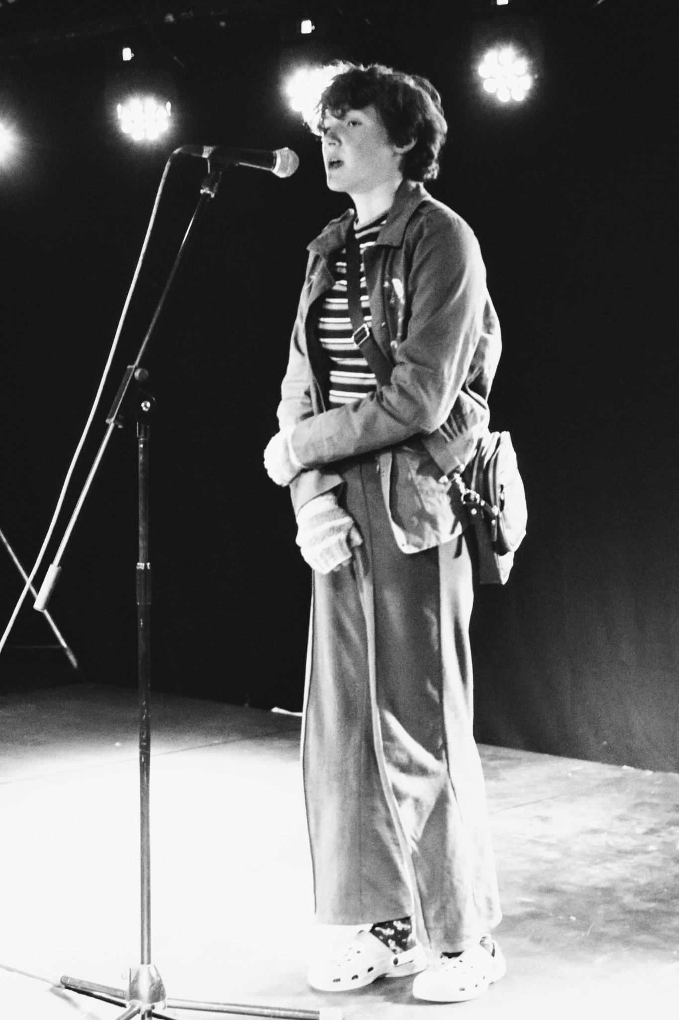 Black and white photo of a young person standing in front of a microphone on stage