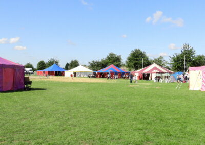 Wide angled shot of a large field with six marquees in bright colours, some are striped. There are people walking around in the distance
