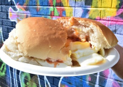 Photo of a breakfast bread bun with egg on a paper plate and a bright wall of graffiti in the background