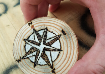 Close up photo of a wooden disc with a compass design on it made by a pyrography tool