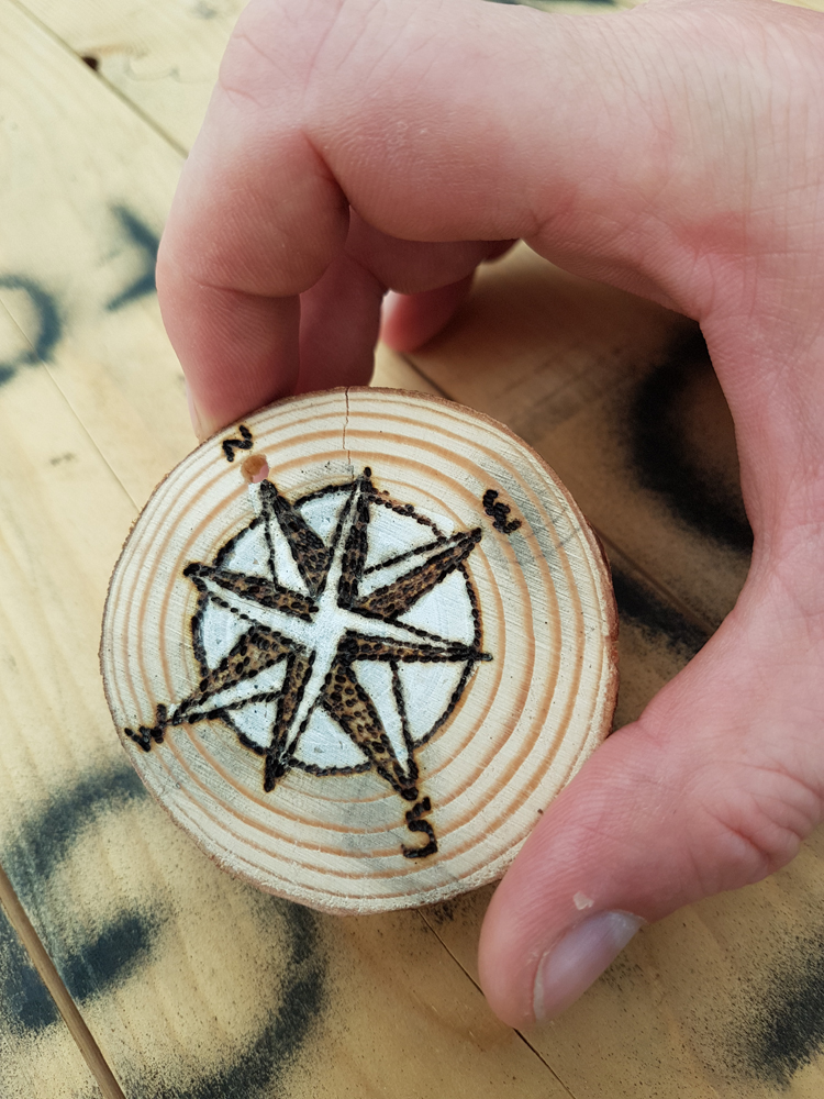 Close up photo of a wooden disc with a compass design on it made by a pyrography tool