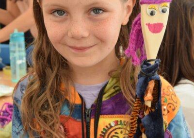 Photo of a young girl smiling for the camera while holding up a doll made from a wooden spoon