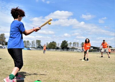 Photo of a group of people wearing orange vests and playing rounders in a field