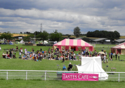 Wide angled photo of a field with a large stripy marque and a large group of peopke taking part in a tie dyeing session on the grass