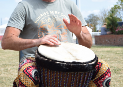 Photo of a man sat outside playing a West African drum