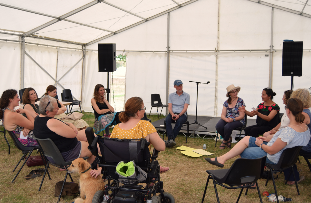 Photo of a group of people sat on chairs in a marquee facing a man sitting on a small stage facing them