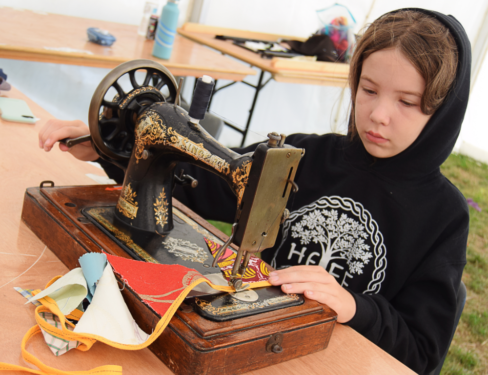 Young person sat in front of a handcrank sewing machine