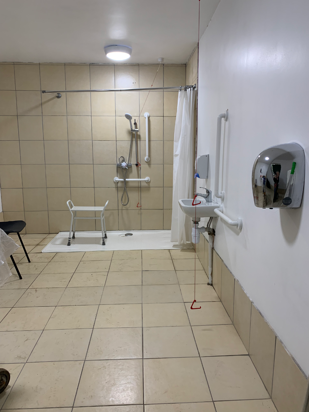 Photo of the accessible shower room with level access to the shower, a shower stool, sink, hand drier and several grab rails